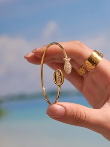 Detail view of gold shell and pineapple pendants with stones on a steel open cuff bracelet