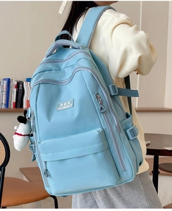 Detail view of light blue multi-pocket backpack with plush puppy charm on model