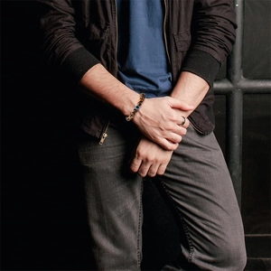 Detailed close-up of men's brown tiger eye bracelet with blue evil eye bead on wrist