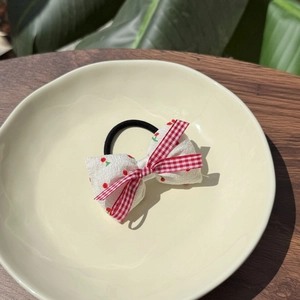 Detail of red checkered bow hair scrunchie with cherry print in a ceramic dish