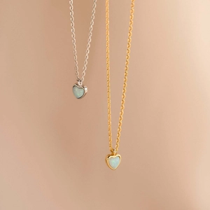 Macro detail of gold and silver heart necklaces with iridescent white opal inlays