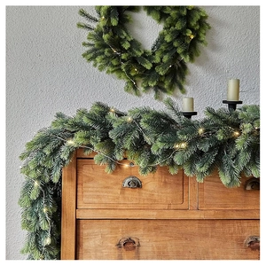 Detailed view of artificial pine garland and wreath with warm LED lights on a wooden cabinet