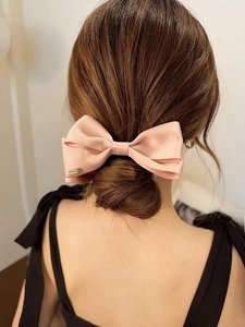 Macro detail of large pink satin bow hair claw clip with elegant silk texture and gold label