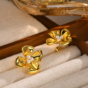 Elegant gold flower stud earrings with pearl centers on a beige velvet jewelry display