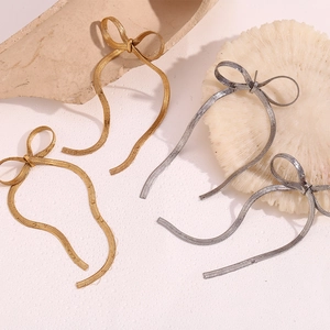Detailed shot of bow knot earrings in gold and silver hanging over coral decor
