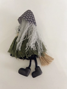 Detail of handmade Halloween witch doll with grey hair and a small straw broomstick