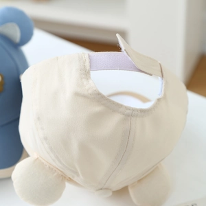 Détail de l'attache velcro et des oreilles en peluche sur la casquette en coton beige bébé