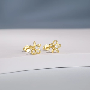 Close-up of golden flower stud earrings with center crystals on a soft blue background