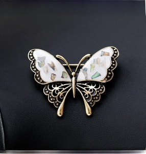 Detailed macro view of a gold butterfly brooch with iridescent shell wings on black leather