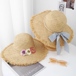 Détail de chapeau de paille à large bord avec fleurs à la main et chaîne de perles