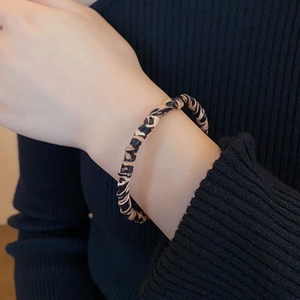 Detail view of the leopard print leather twisted bangle on a black knit sleeve
