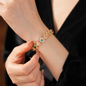 Macro shot of gold bracelet featuring heart-shaped colorful zircons worn on wrist