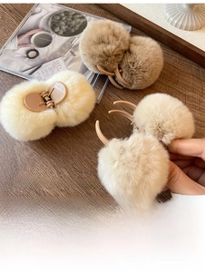 Detail view of plush pom-pom hair claws in cream and brown on a wooden background
