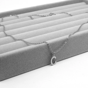 Close-up of silver stainless steel letter C pendant necklace on a grey velvet tray