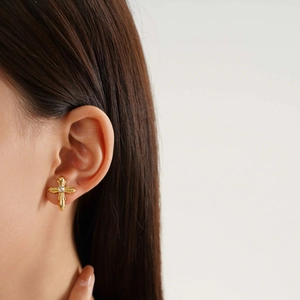 Close-up of gold-plated cross stud earring with white crystal on model ear