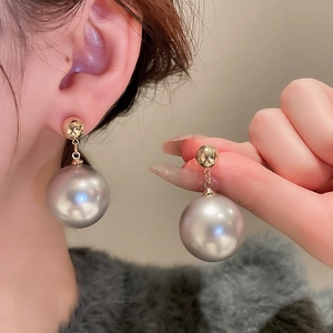 Elegant gold earrings with large grey pearls shown on model and held in hand