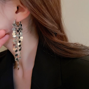 Close-up of long silver metallic sequin fringe earrings worn by a model