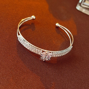 Detail of silver double-layer open bangle with zircon pavé and geometric flower charm