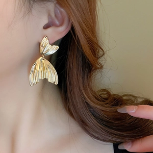Close-up of golden fishtail earrings with vertical texture on model's ear