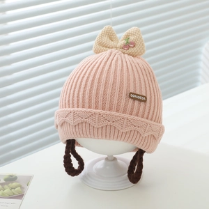 Détail du bonnet en tricot rose pour bébé avec broderie cerise et nattes tressées