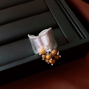 Detail of irregular silver wrinkled band ring with amber-colored beaded charms on black tray