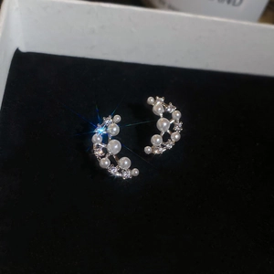 Detailed view of silver crescent earrings with white pearls and sparkling zircons on velvet