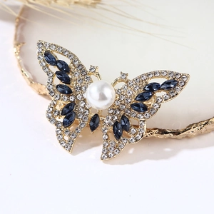 Elegant gold butterfly brooch with large center pearl and blue gemstone wing accents