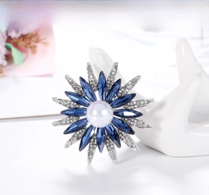 Dettaglio spilla a girasole con pietre blu e perla su un modello di mano in ceramica