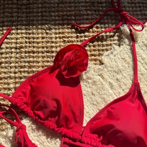 Detail of red bikini top featuring 3D rose applique and halter neck on beach mat