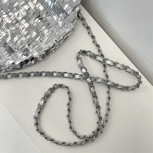 Detail of silver sequin handbag with polished metal chain strap on textured surface
