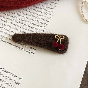 Macro shot of plush brown triangular hair clip with red cherry and gold metal bow detail