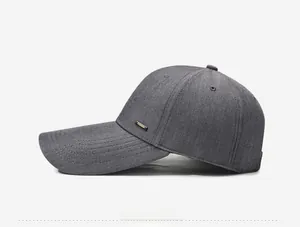 Detail view of grey baseball cap showing long brim stitching and fashion metal badge