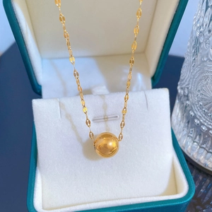 Macro shot of gold spherical pendant on a flat link chain inside a green jewelry box
