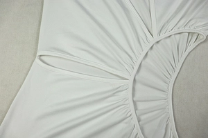 Detail shot of white fabric featuring intricate cutout designs and pleated textures