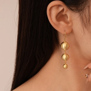 Macro detail of triple gold ball drop earrings with elegant brushed metal texture finish