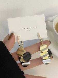 Detail of long fringe earrings with tricolor metal discs in gold, silver, and black