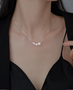Detailed close-up of four gradient pearls on a fine silver chain worn with black outfit