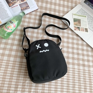 Détail d'un sac bandoulière en toile noire avec motif de visage de dessin animé blanc