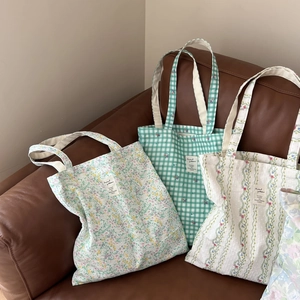 Three canvas tote bags with green floral and plaid patterns on a leather sofa