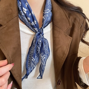 Close-up of a blue paisley silk scarf necklace knotted over a brown suede blazer