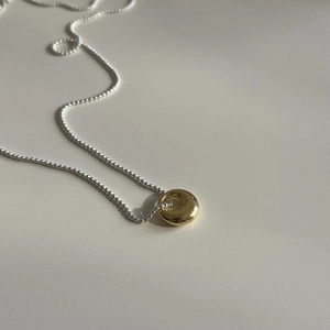 Detail of high-polish gold donut pendant and silver ball chain with light shadow