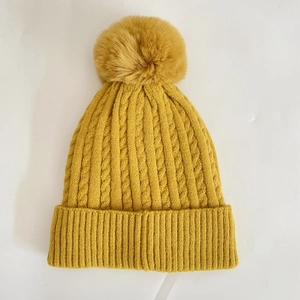 Detailed close-up of a mustard yellow winter knit beanie with a fluffy faux fur pom-pom