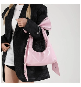 Pink patent leather half-moon shoulder bag with studs and large bow detail shown on model