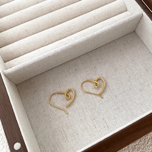 Detailed close-up of gold heart stud earrings with twisted texture in a jewelry box