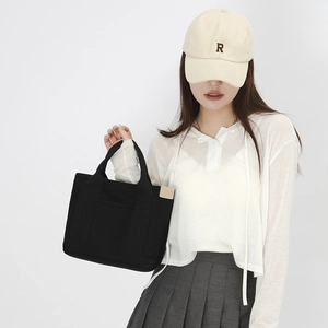 Fashionable black canvas handbag shown with a minimalist outfit and pleated skirt