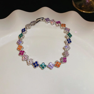 Detail shot of a silver clover bracelet with colorful zircons on a white ceramic plate