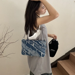 Detail of blue denim shoulder bag with frayed tassels and metal chain strap details