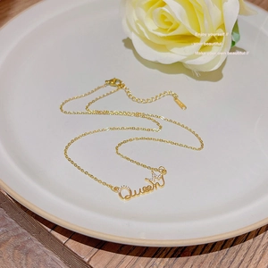 Elegant gold Queen pendant necklace with crown design and zircons on a white plate