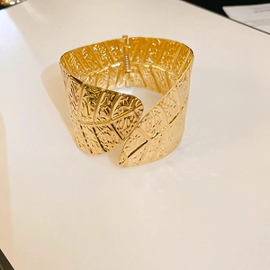 Wide gold metal bangle featuring embossed leaf vein texture and a hinged clasp