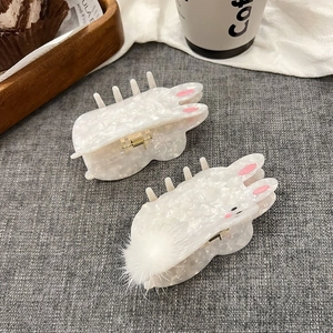 Detail of cute rabbit hair claws with white marble texture and soft plush pompom
